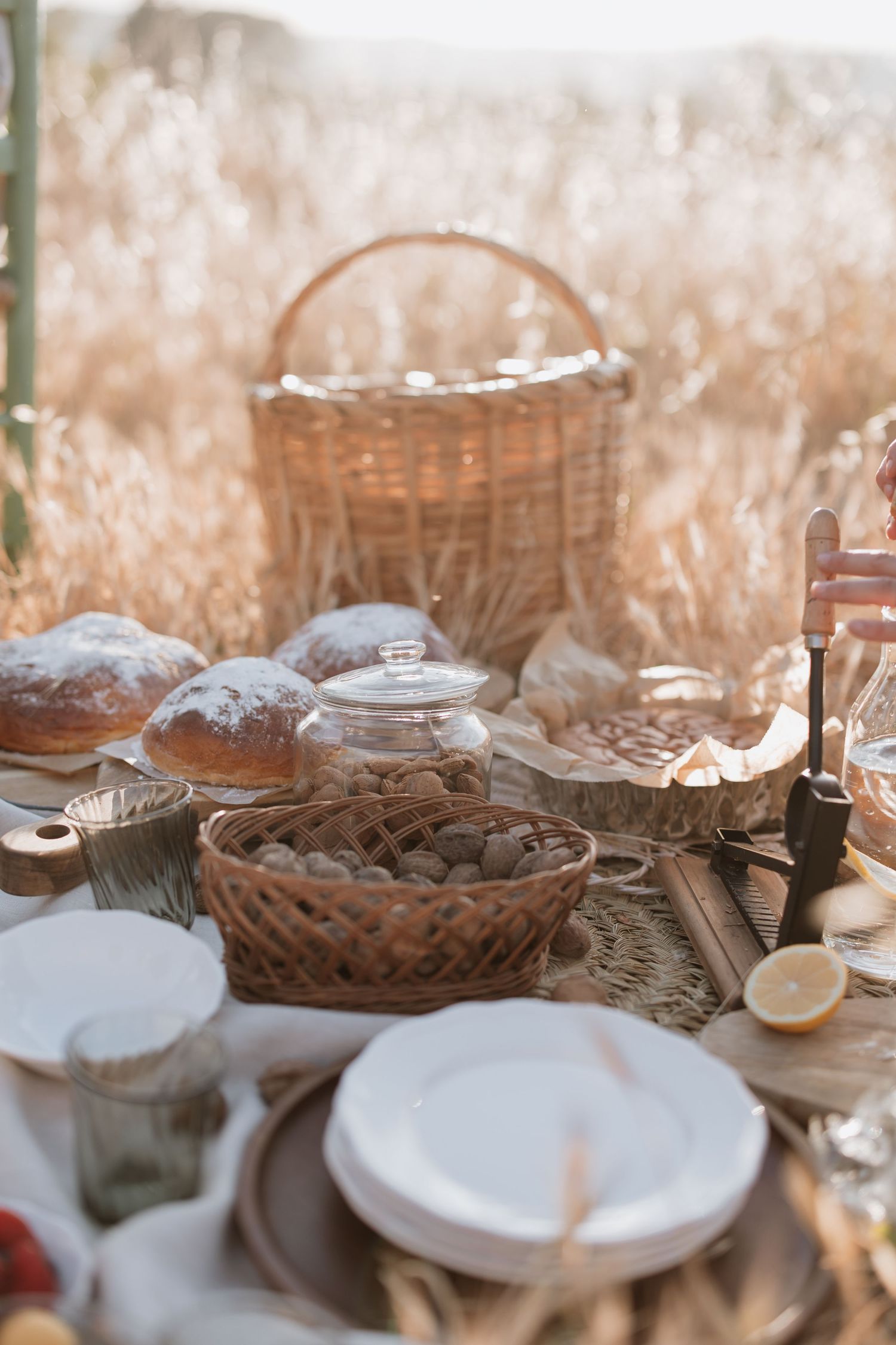 Rustic table setting with woven baskets and ceramic plates in warm sunlight against a blurred wheat field background.
