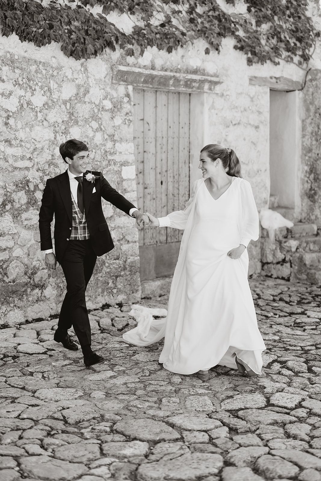 Black and white photo of couple dancing on cobblestone path by rustic door.