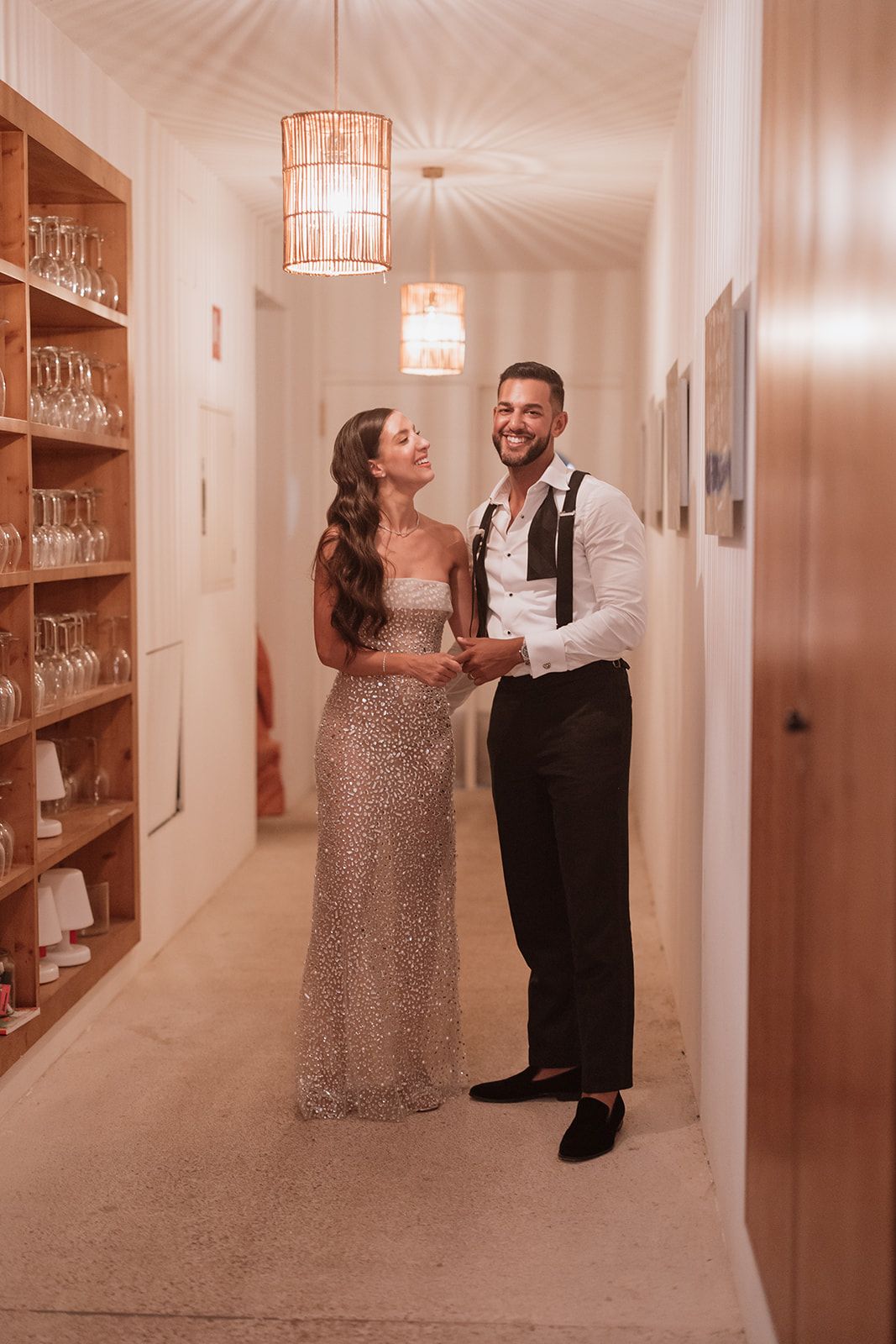 Couple sharing intimate moment in hallway with sparkly dress and formal attire.