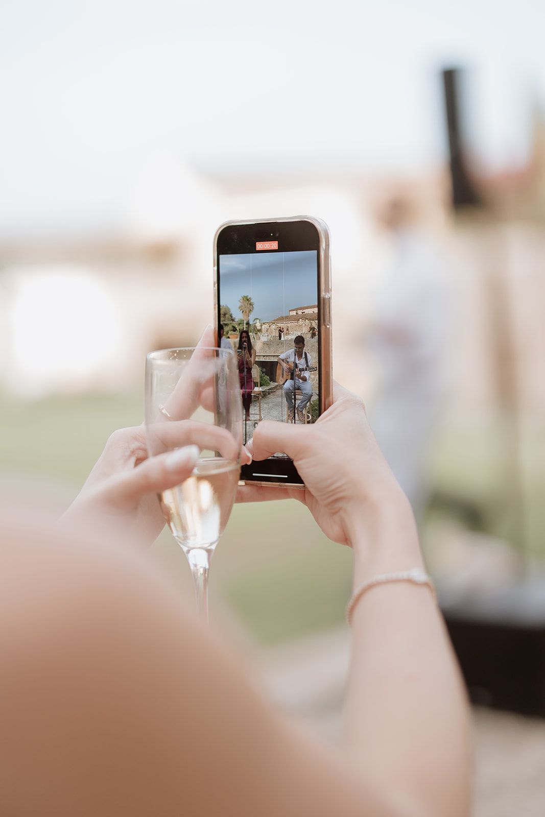 Hands holding a smartphone to capture wedding moments at an outdoor venue.