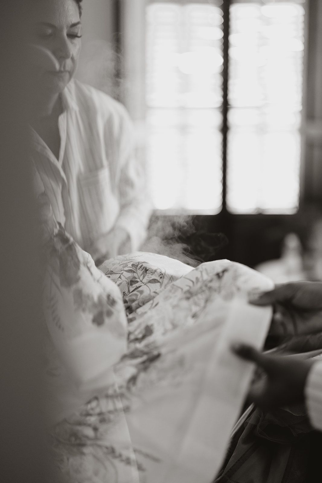 Artistic black and white photo showing hands with rising steam in soft window light.