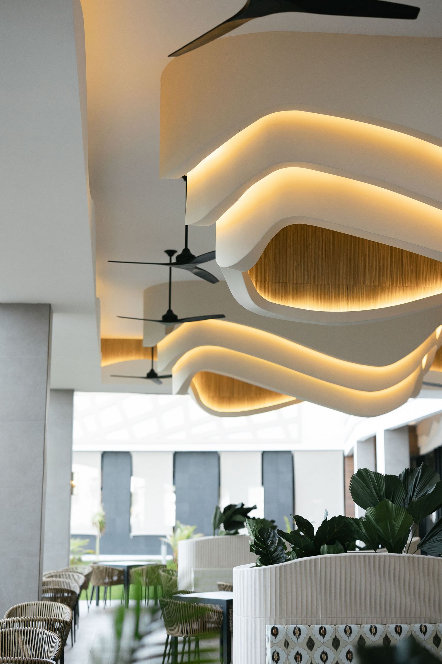Modern restaurant interior with curved illuminated ceiling design and contemporary decor featuring hanging ceiling fans.