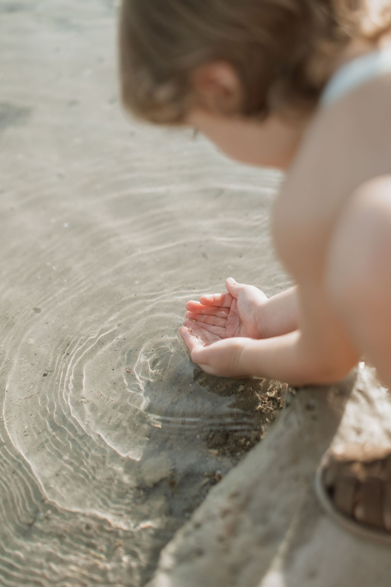 Close-up of small hands touching rippling water surface.