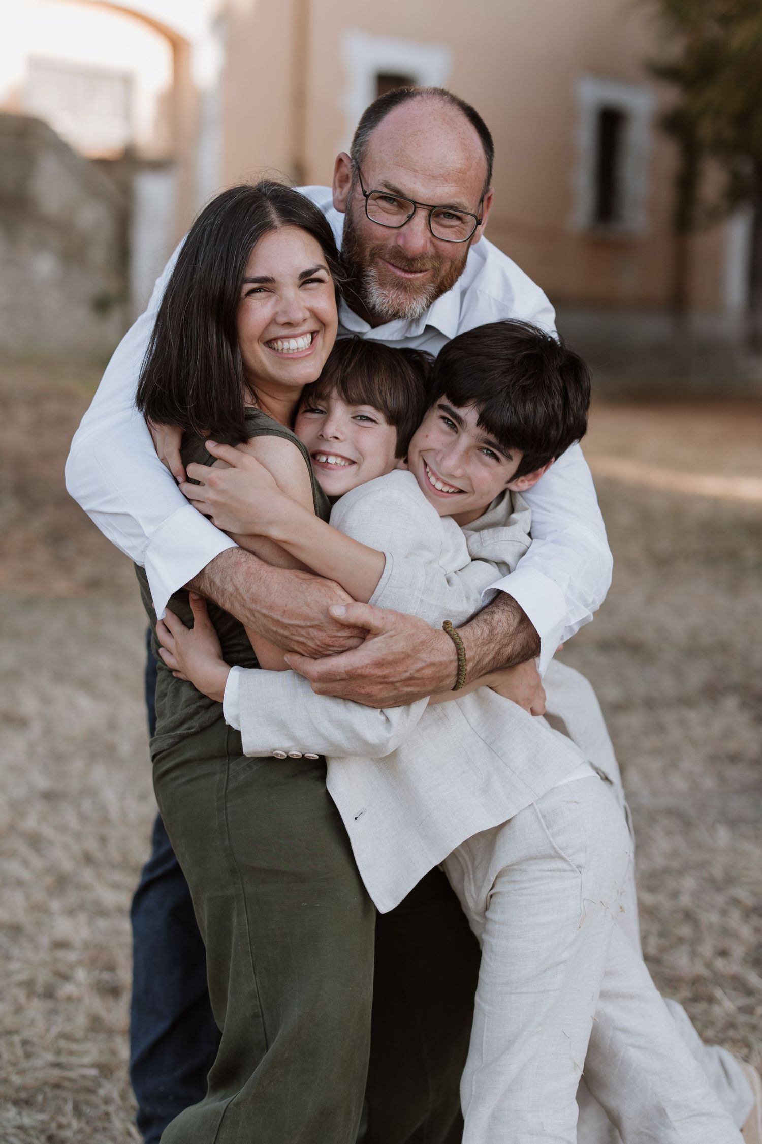 A casual family embrace outdoors with everyone wearing casual clothing in white and olive green colors.