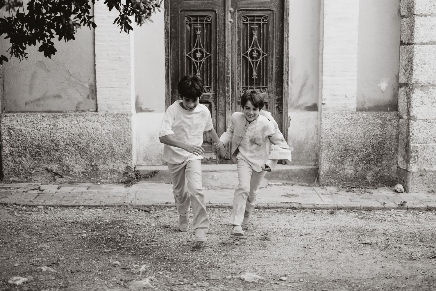 A vintage black and white photograph shows two people sitting casually together on a stone step in front of ornate doors.