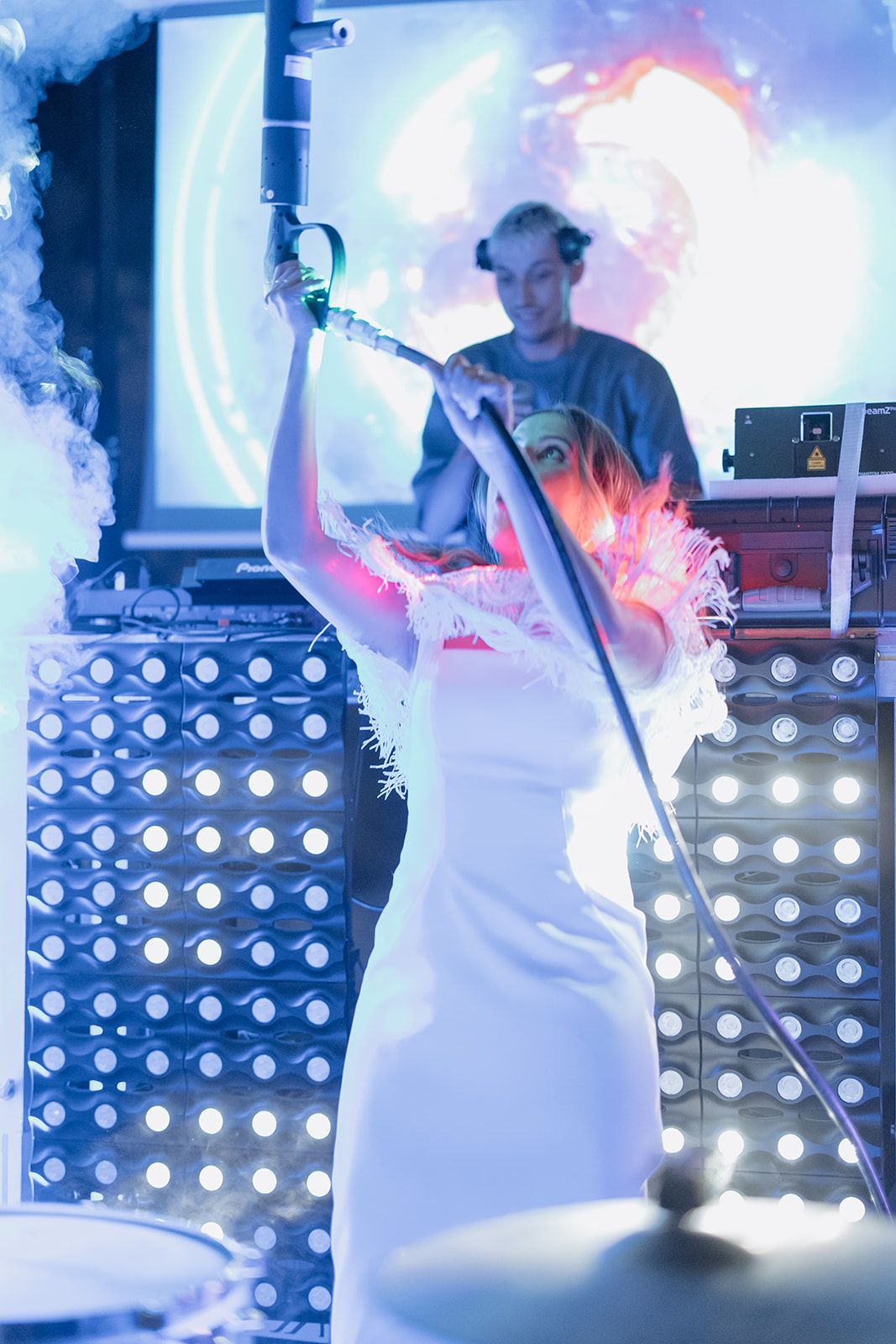 Performer in white dress singing on stage with dramatic lighting and smoke effects.