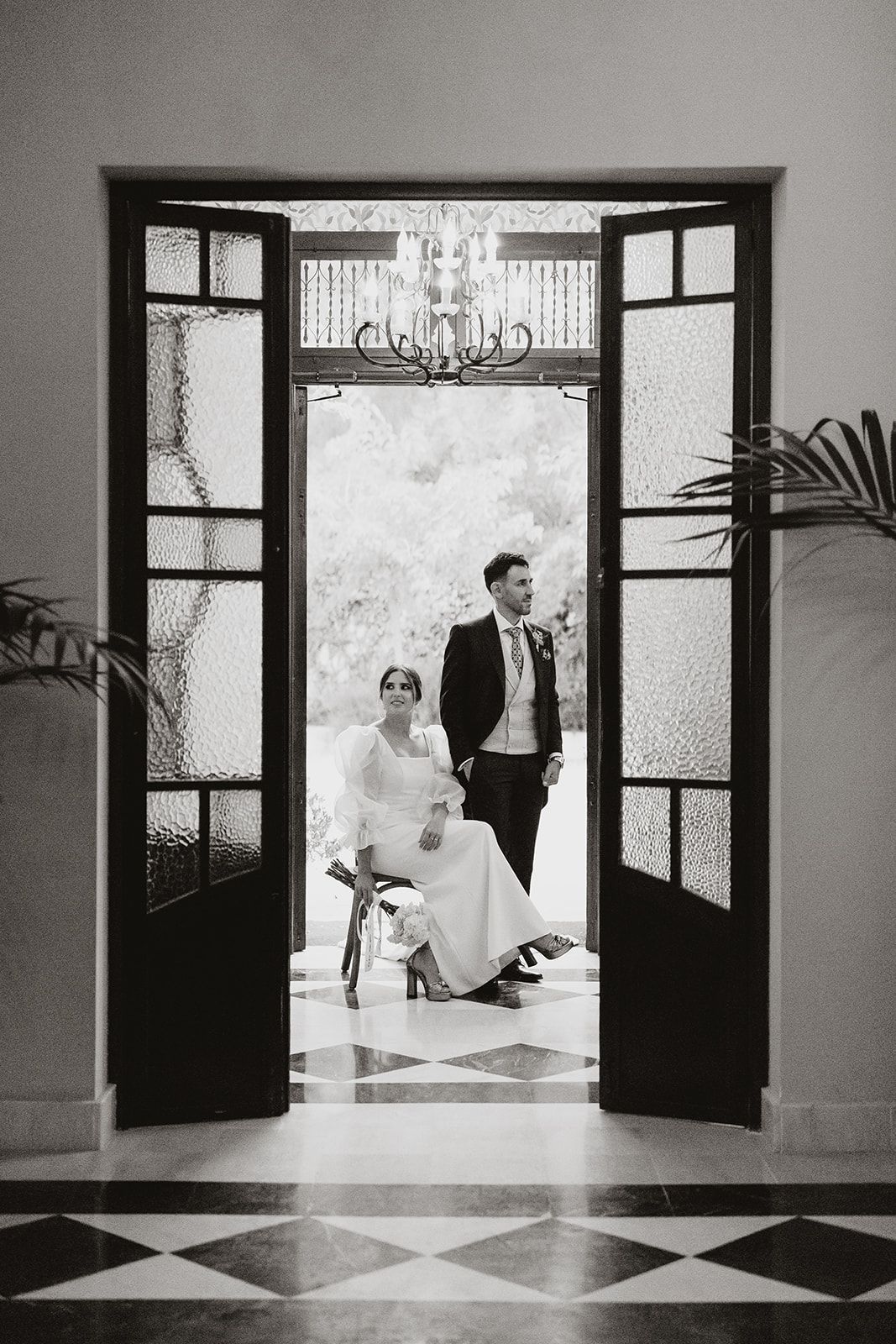 Artistic black and white doorway portrait in elegant venue with chandelier overhead.