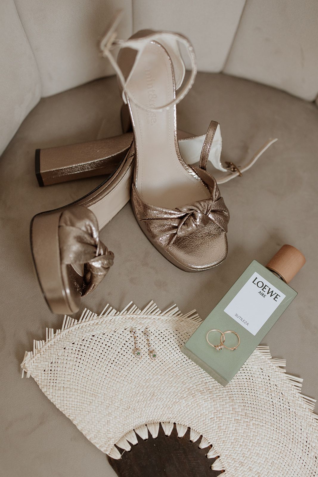 Elegant metallic wedding shoes and rings displayed with a mint green Loewe box on lace fabric.