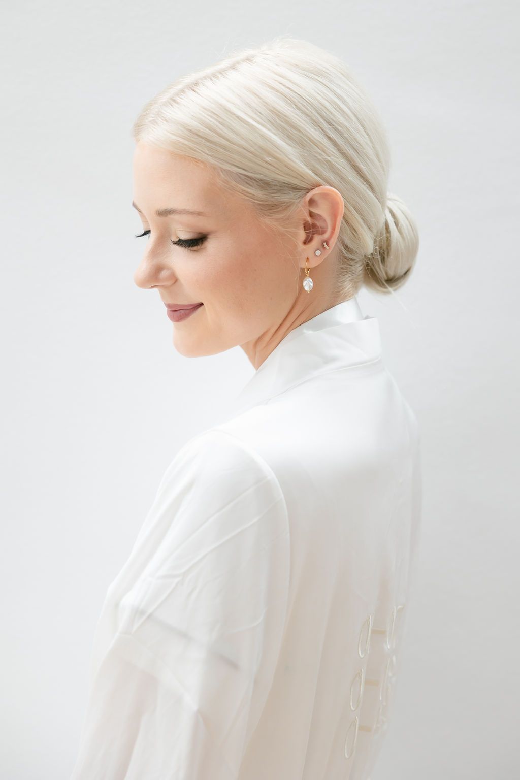 Side profile view of a person in white with elegant updo hairstyle against light background.