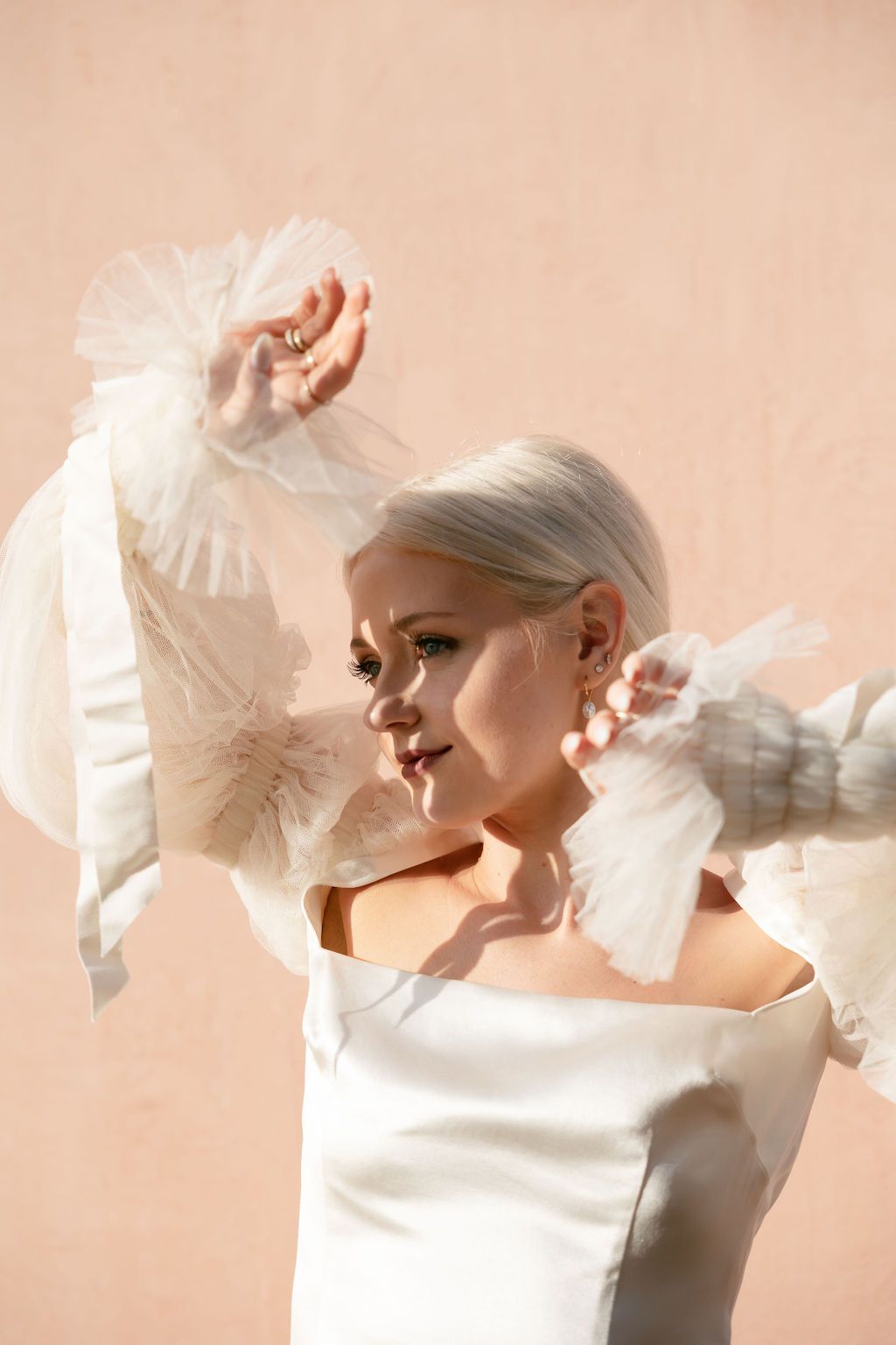Elegant bridal portrait with flowing white fabric details against a soft pink background.