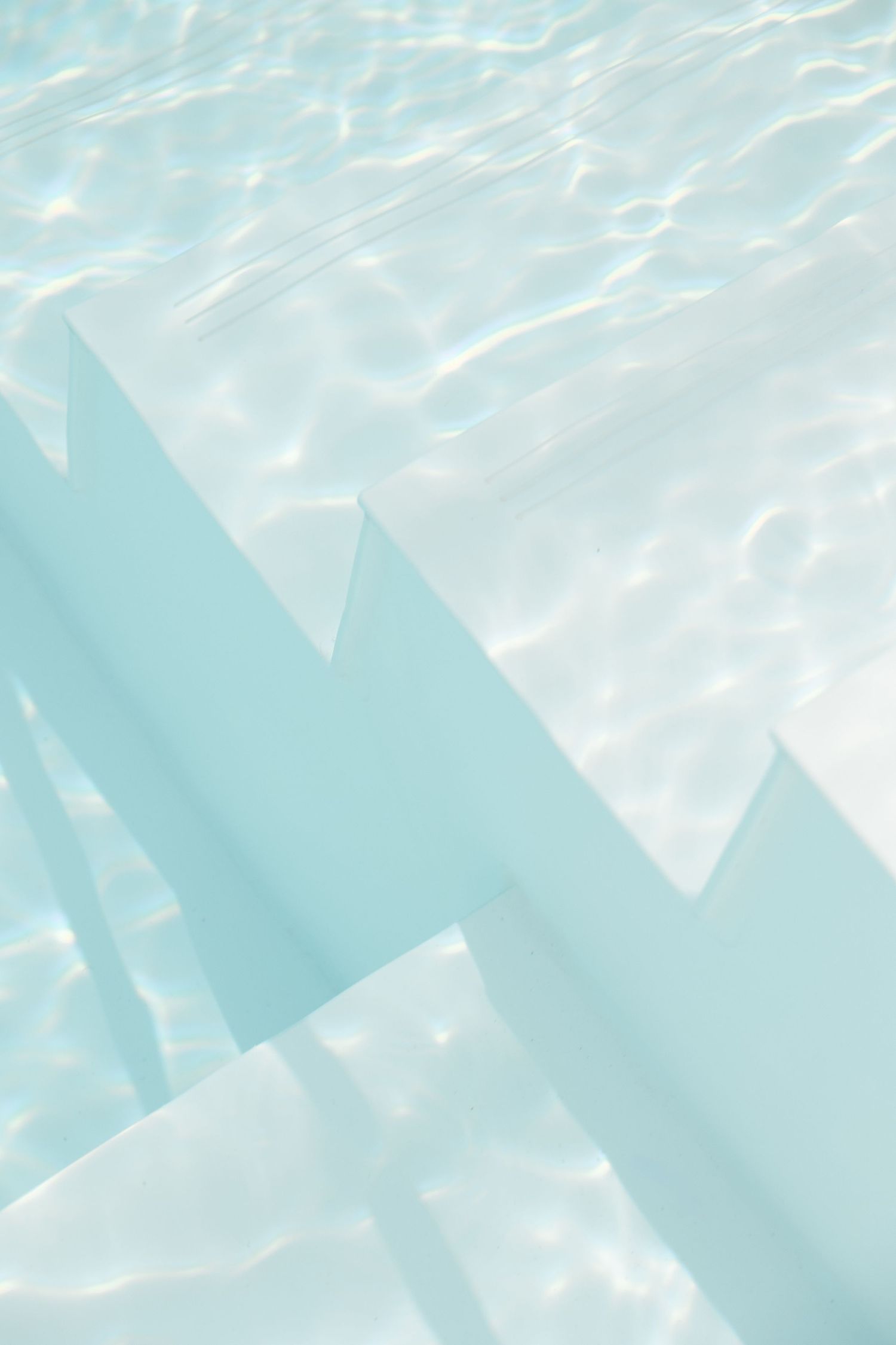 Abstract pattern of light reflecting through pool water in shades of blue and white.