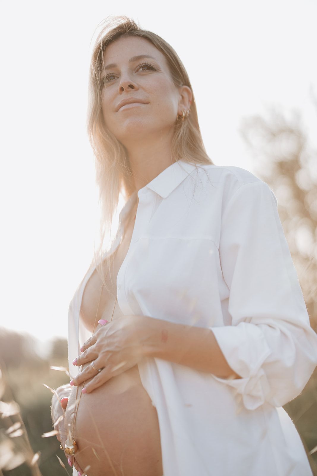Glowing maternity portrait in natural sunlight wearing crisp white button-down shirt.