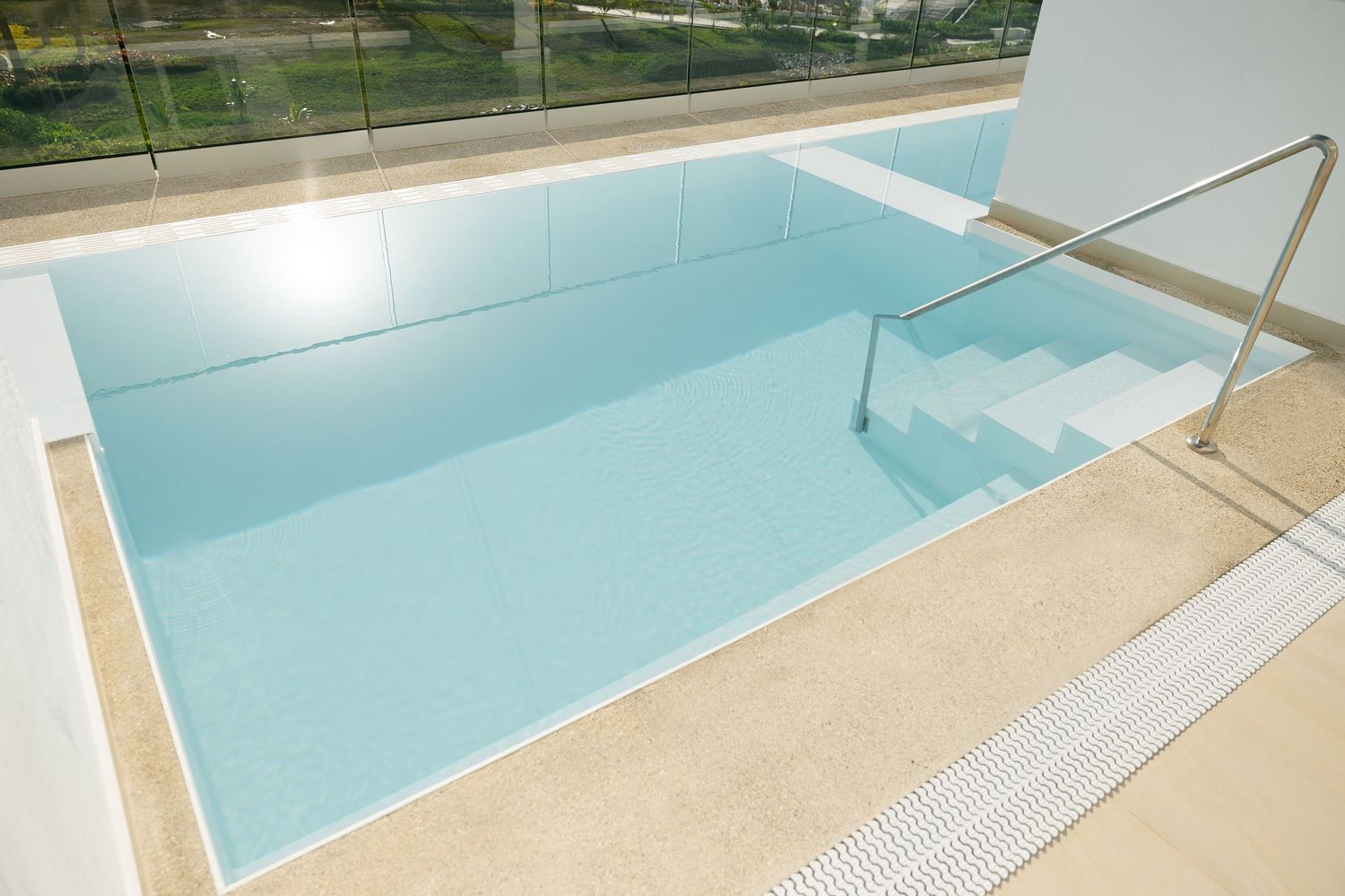 Modern swimming pool with steps and handrail featuring clean geometric design.