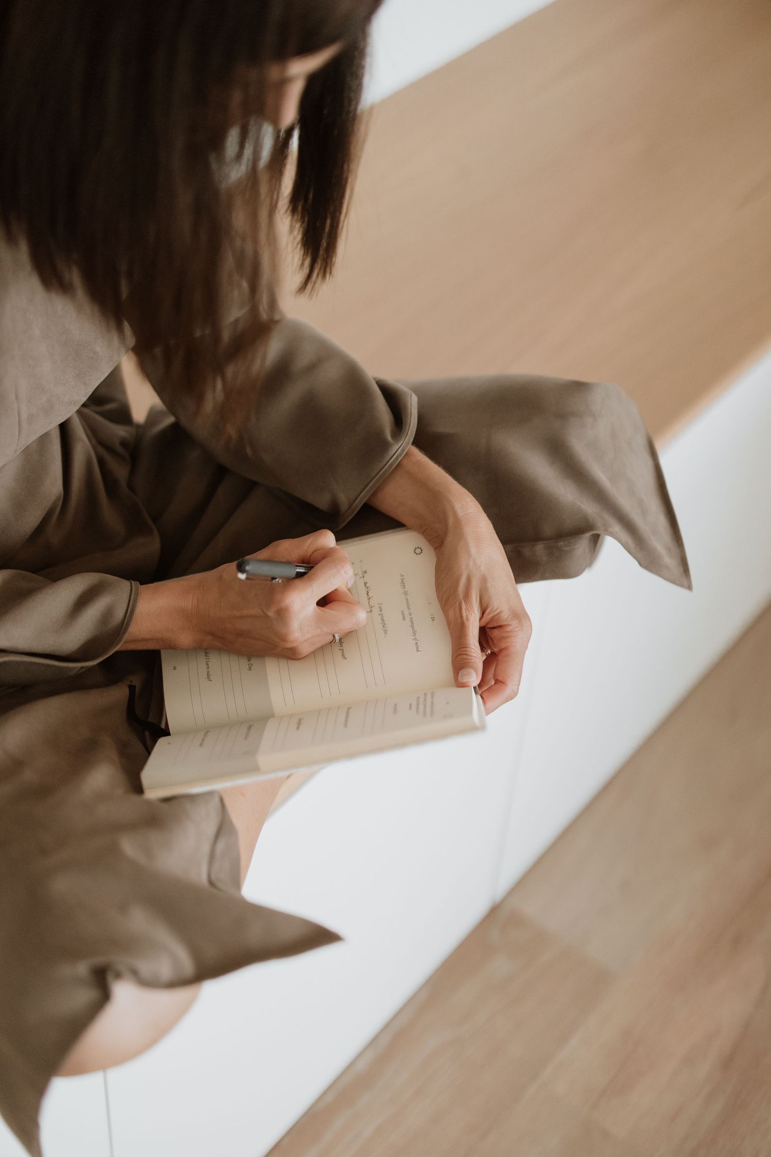 Close-up of hands writing in notebook while wearing flowing brown sleeves.