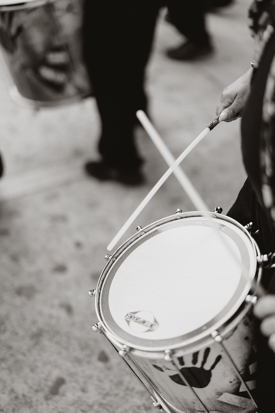 Black and white close-up of drumsticks hitting a snare drum during a performance.