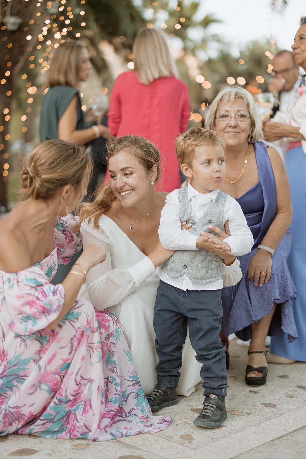 Wedding guests gather outdoors with twinkling lights and palm trees in the background at a celebration.