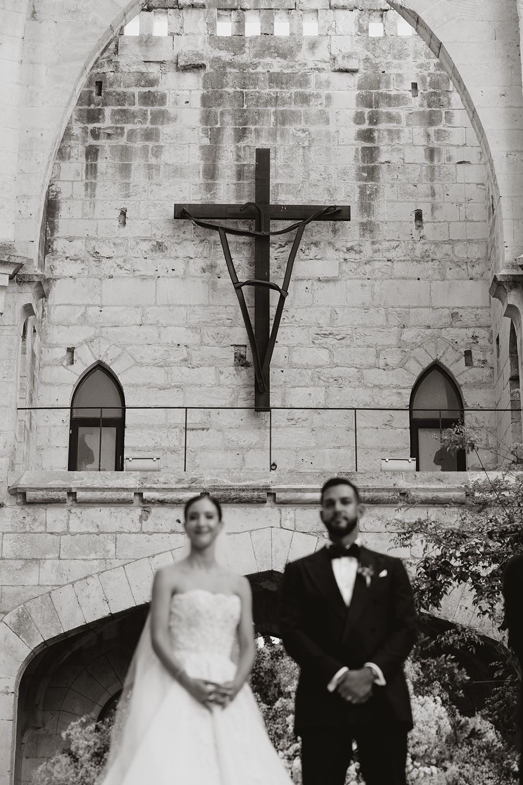 Black and white wedding portrait beneath cathedral crucifix and stone archways.