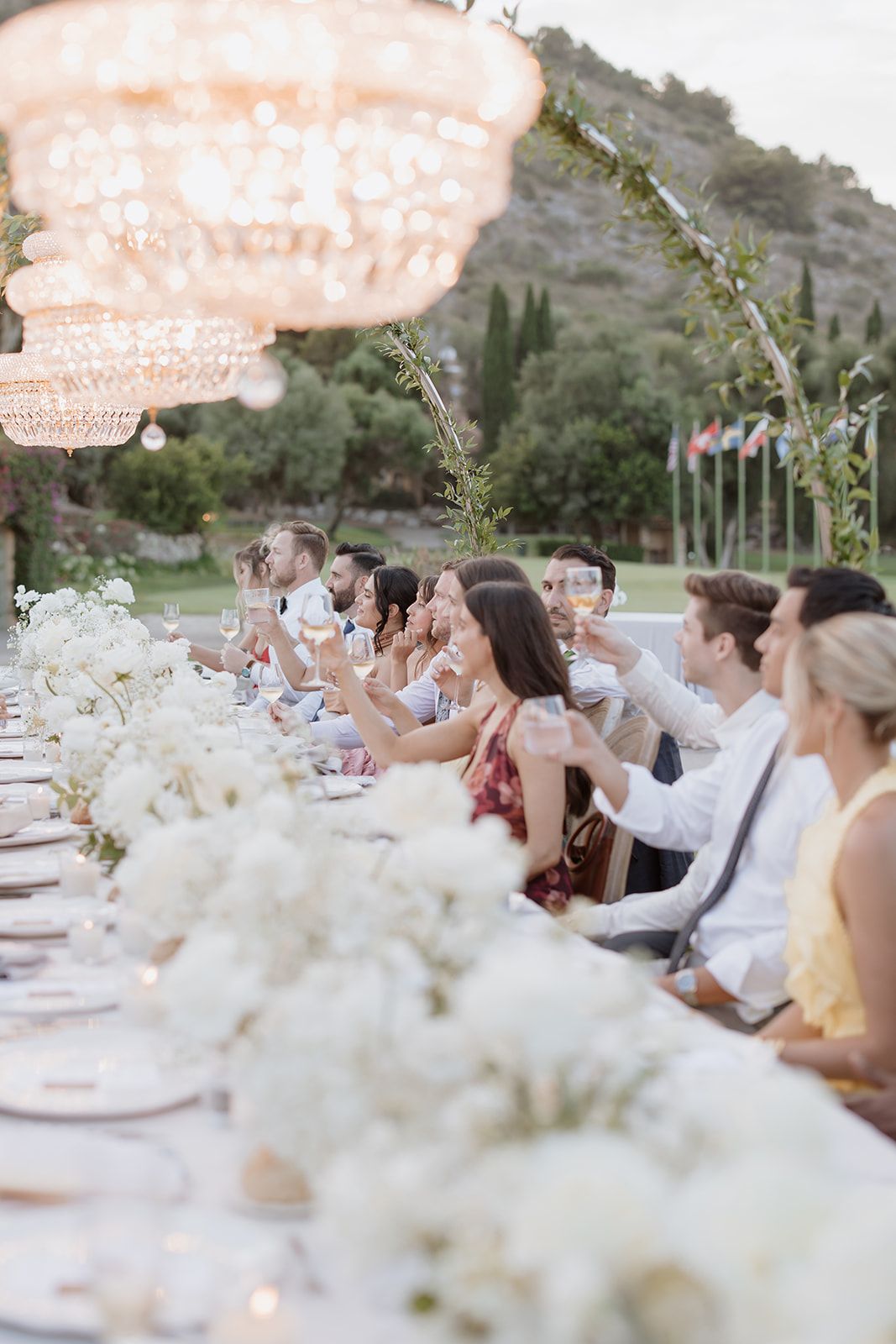 Wedding reception table decorated with white flowers under crystal chandeliers at dusk.