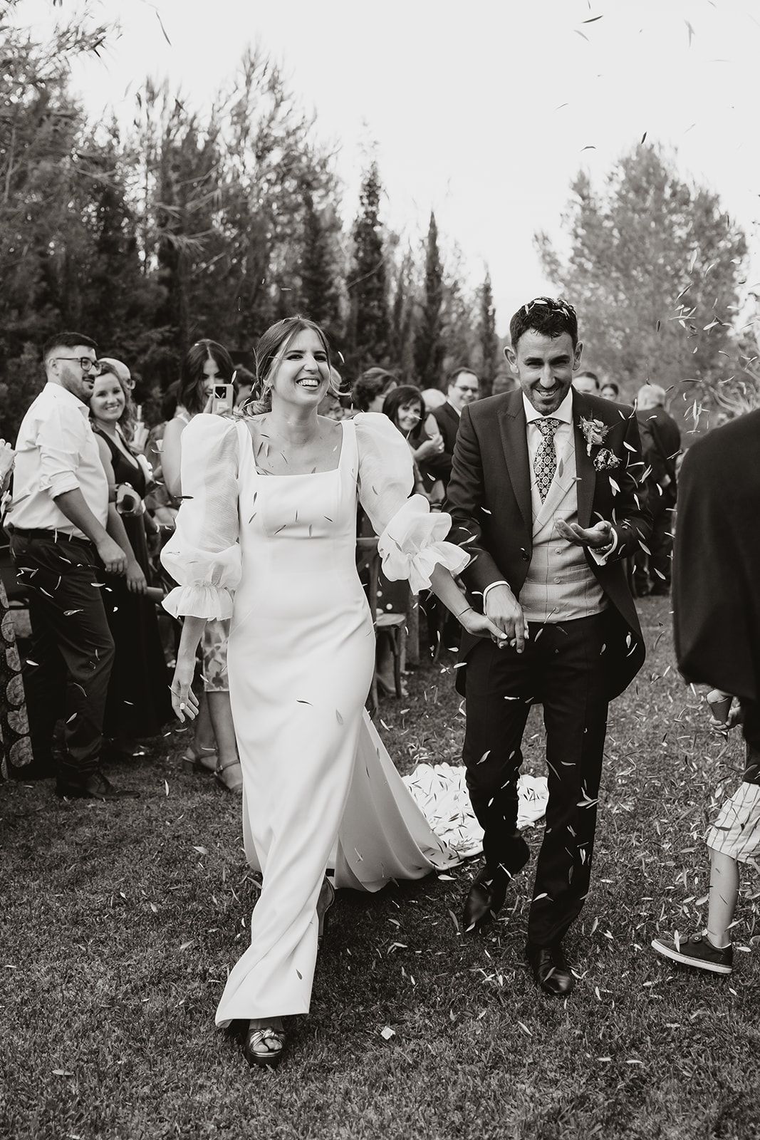 Black and white photo of couple walking through confetti shower at outdoor garden wedding.