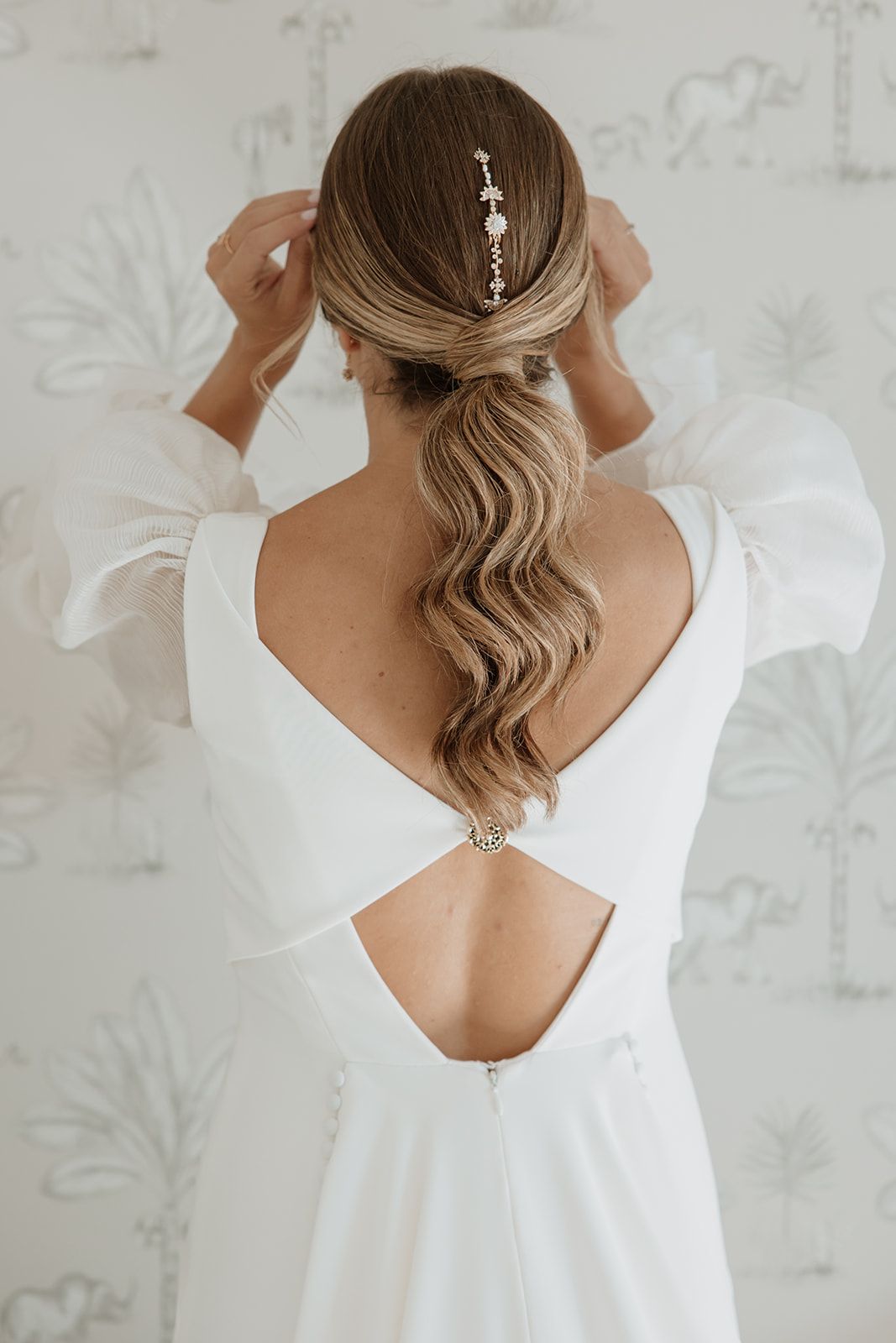 Elegant bridal hairstyle with wavy ponytail and crystal hair accessory shown from behind in white wedding dress.