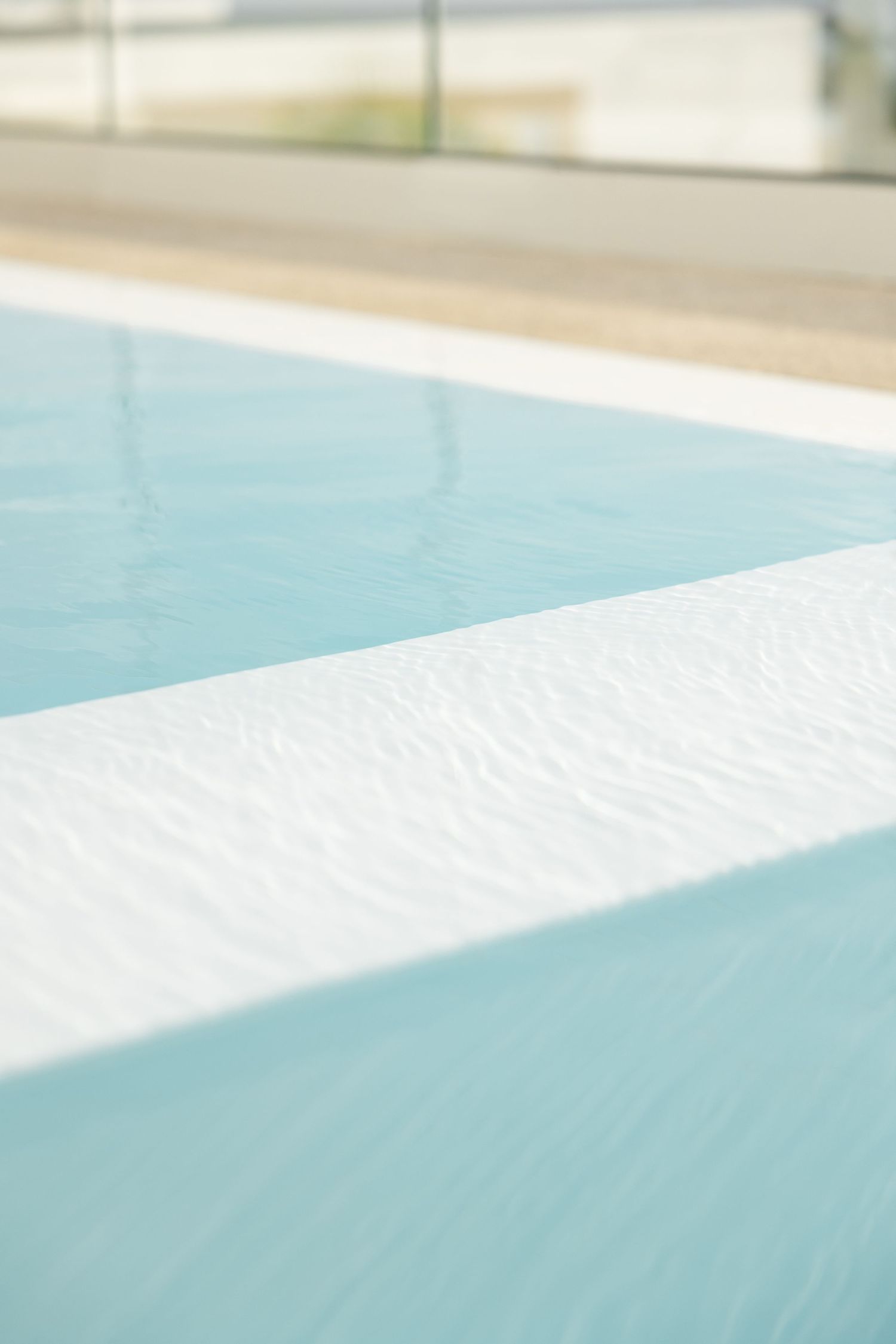 Close-up of swimming pool edge showing clean white tile meeting aqua water.