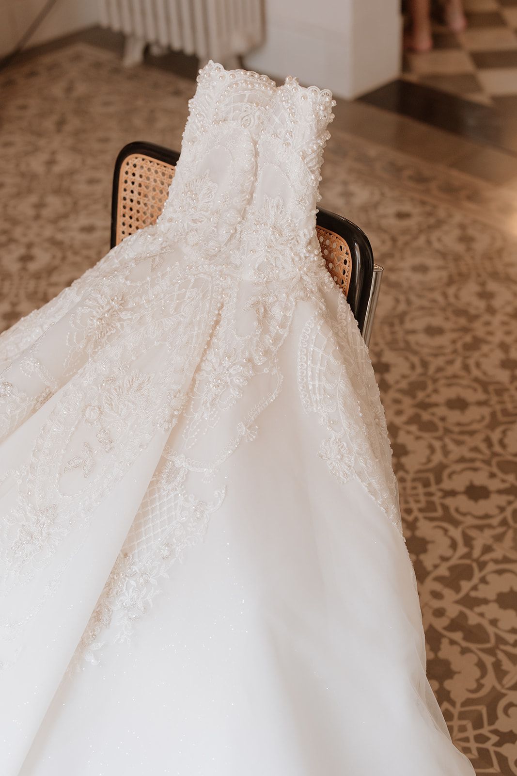 White lace wedding dress draped over vintage cane chair showing detailed beadwork.