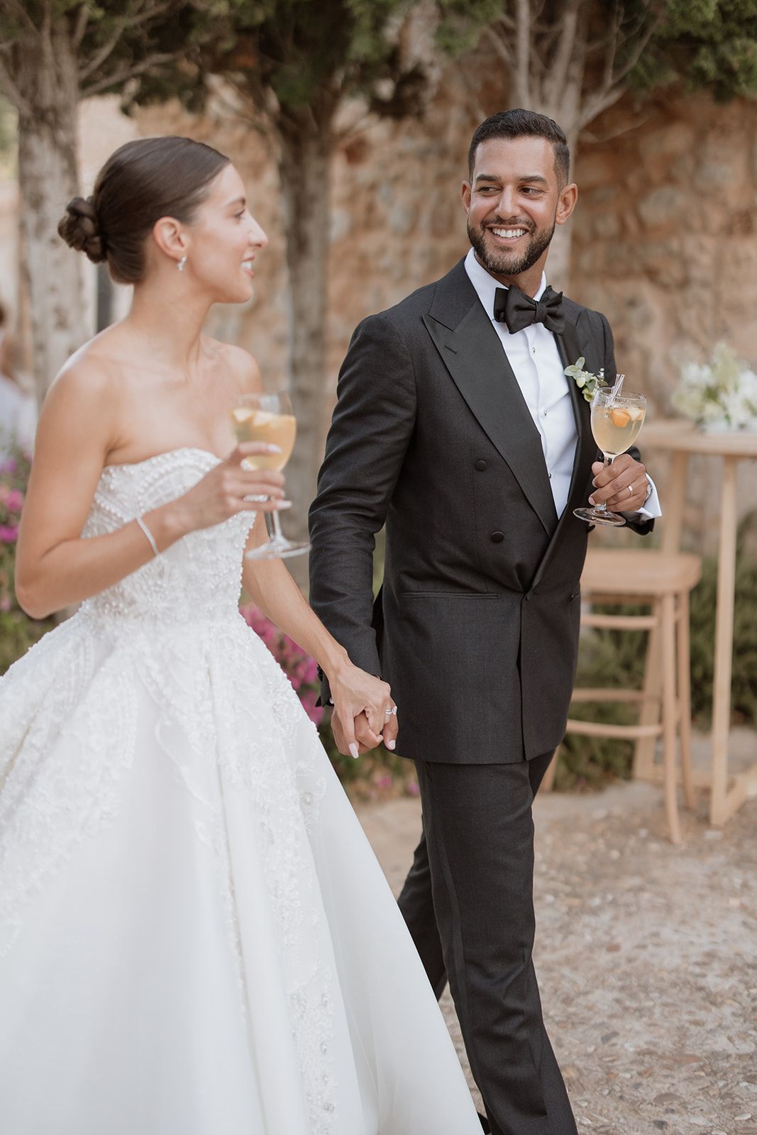 A celebratory moment between newlyweds holding champagne glasses at an outdoor wedding reception.