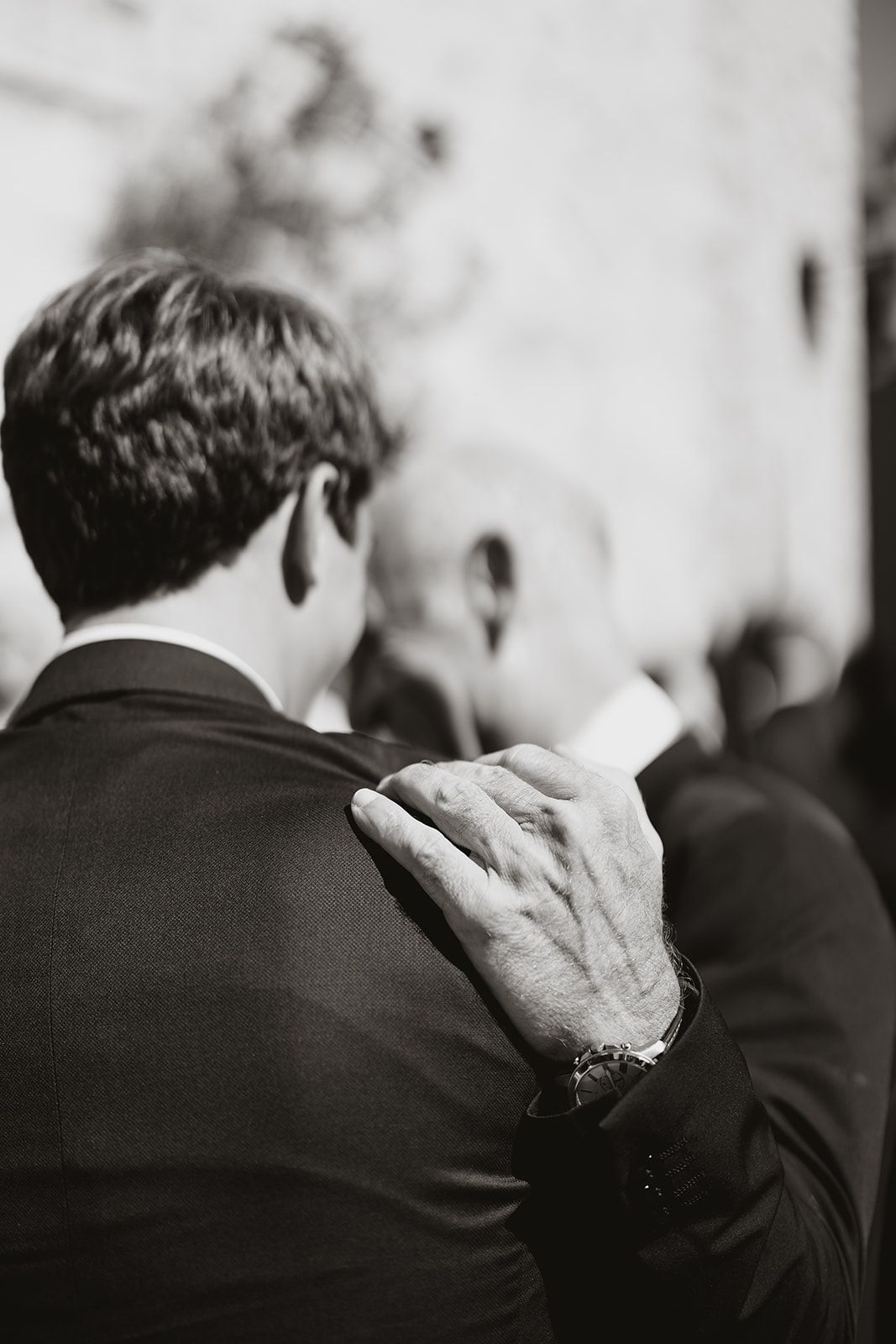 Close-up of hand resting on shoulder in formal black suit.