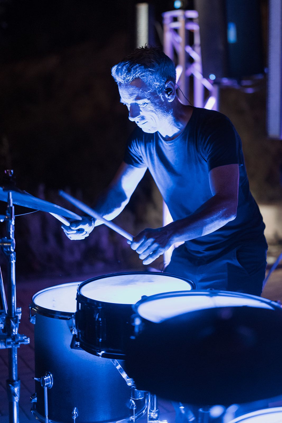 Drummer performing on stage illuminated by dramatic blue lighting.