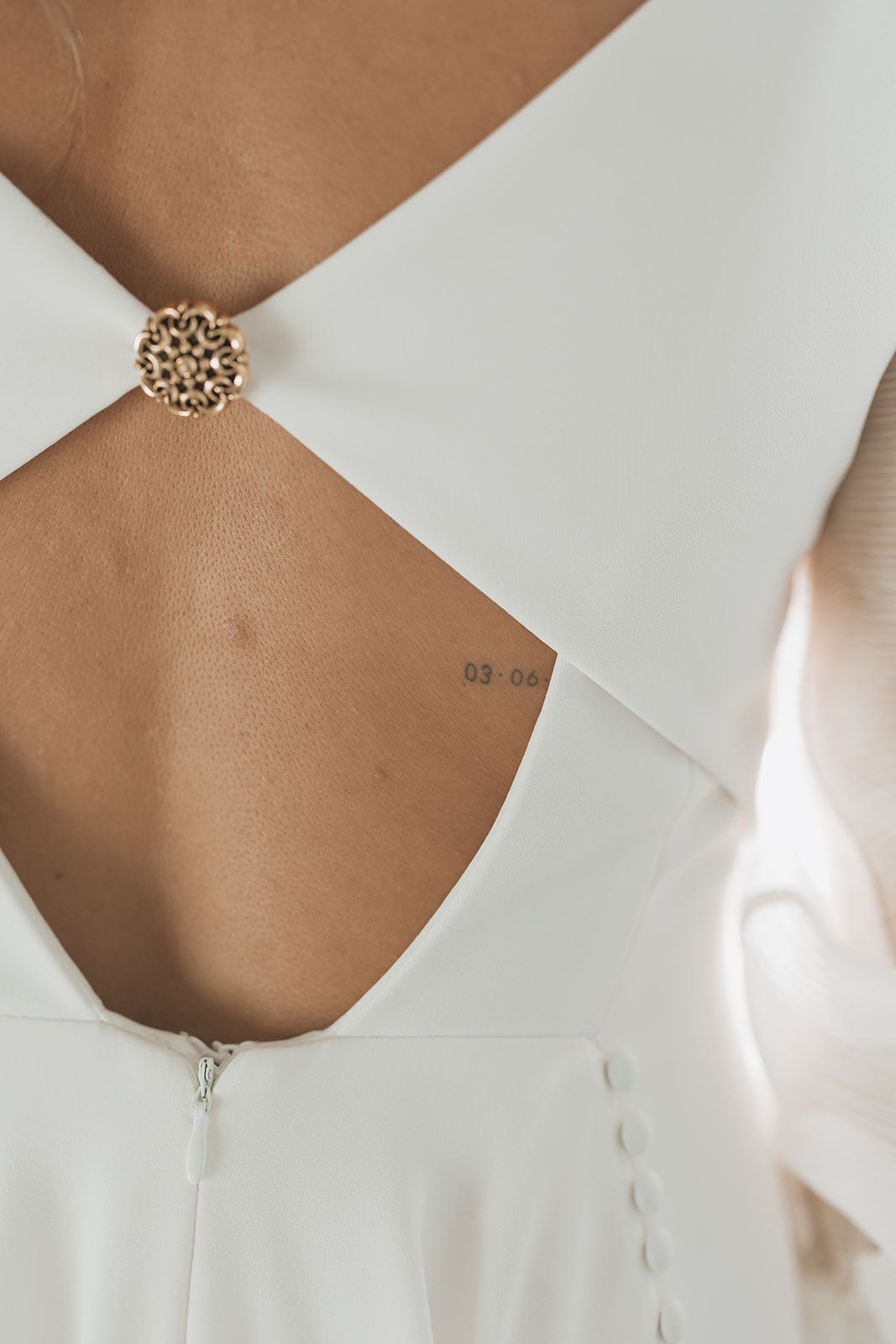 Detail shot of white wedding dress back with ornate gold brooch closure and cutout design.