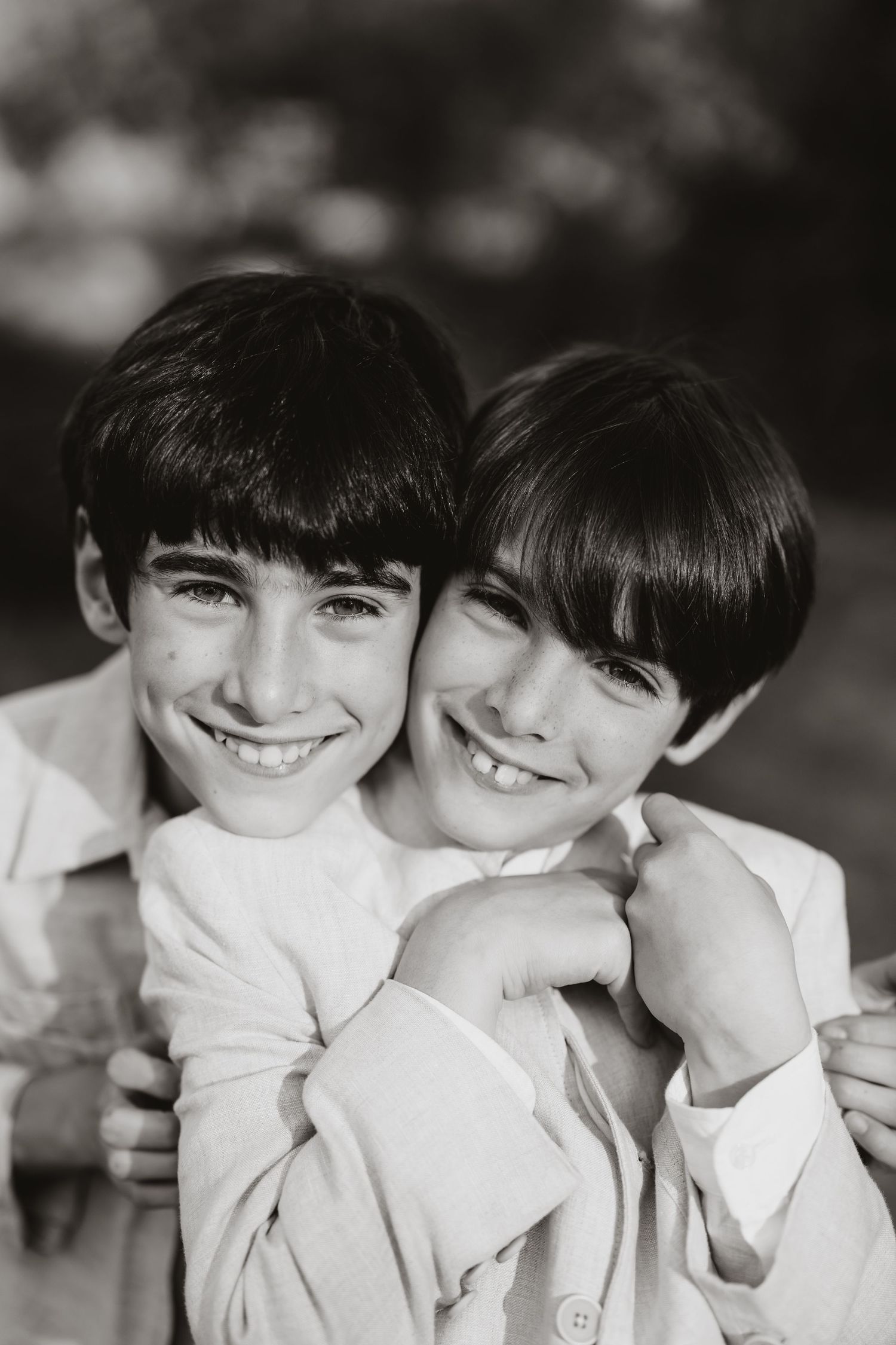 Black and white portrait of young siblings sharing a close affectionate moment while wearing light colored shirts.