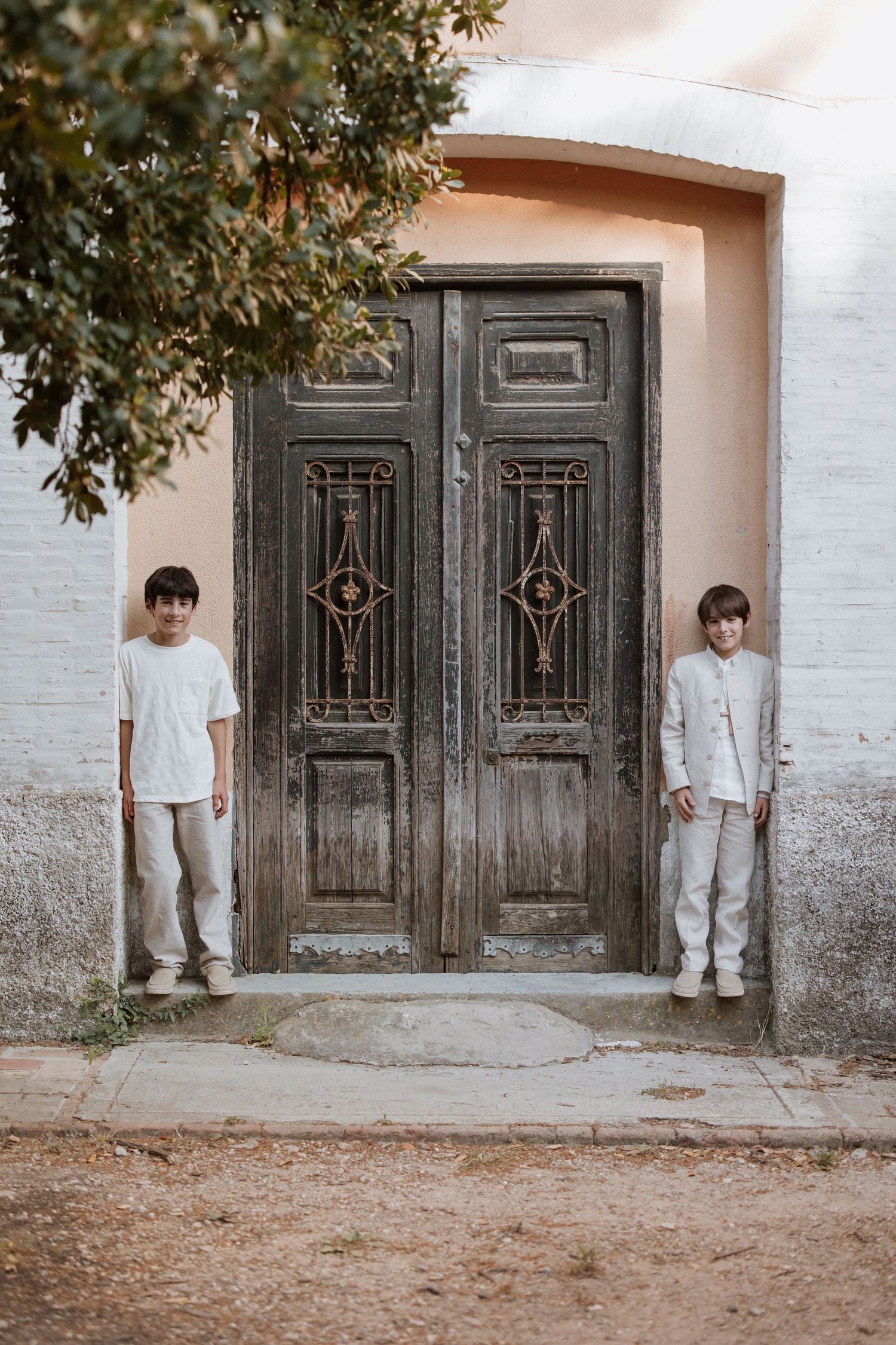 Ornate vintage double doors surrounded by white walls with a tree branch and subjects standing on each side.