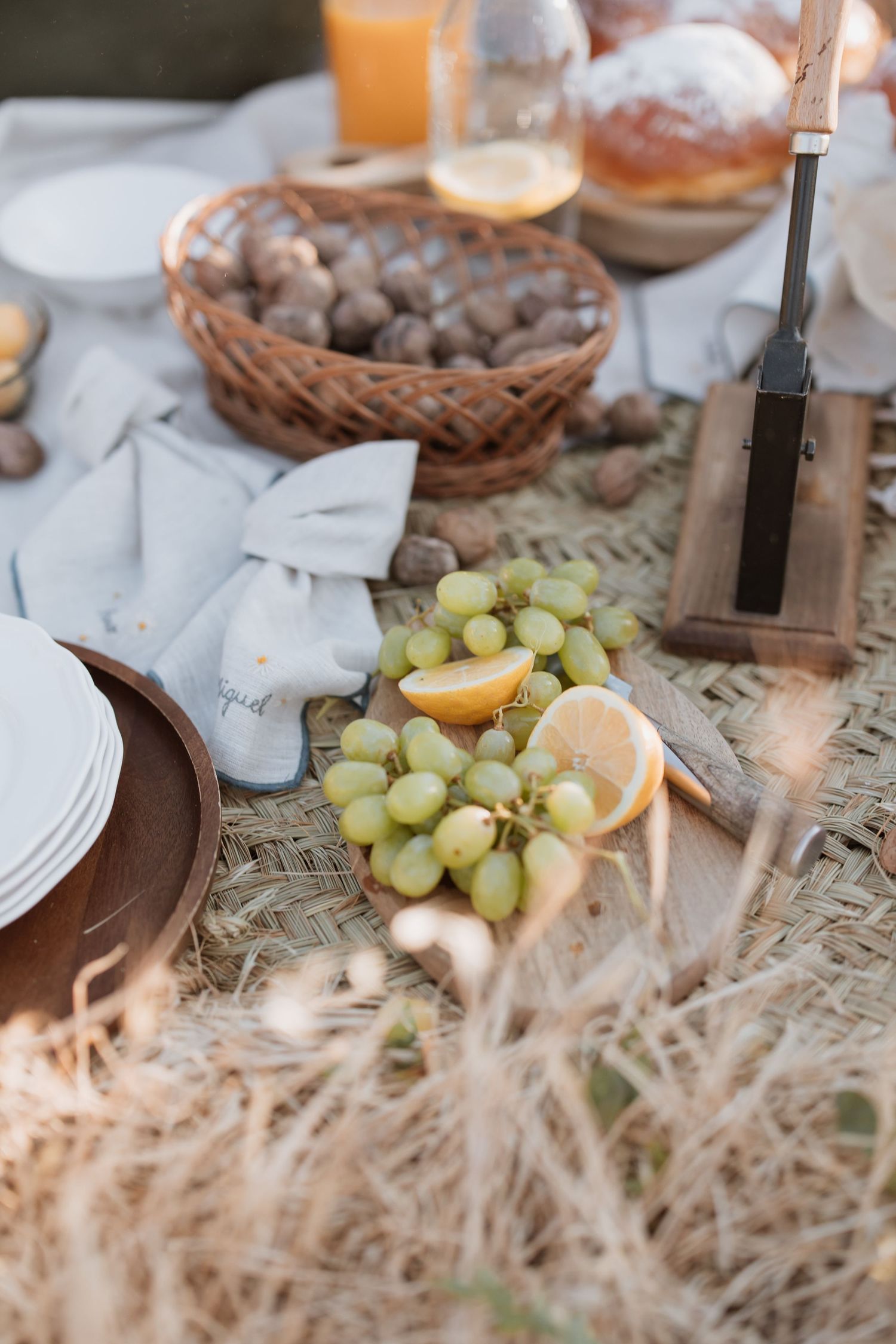 Rustic table setting with fresh grapes, lemon slices, and decorative elements on a textured surface in warm lighting.