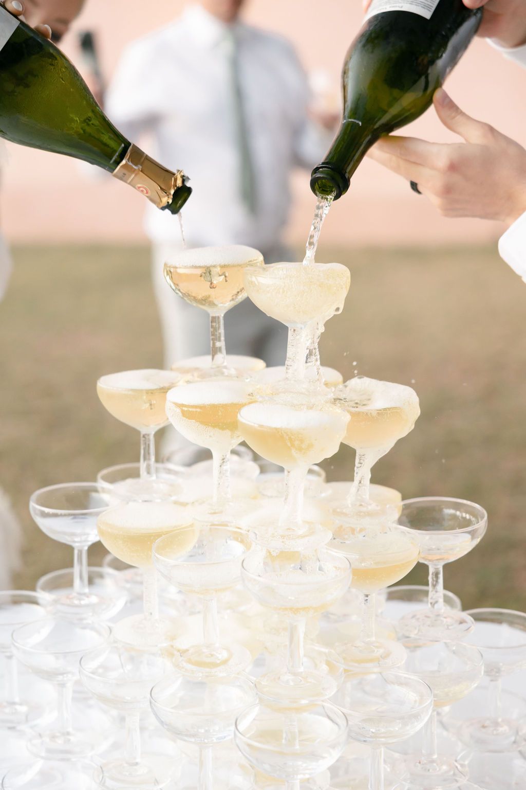Champagne being poured into a tower of coupe glasses stacked in elegant tiers.