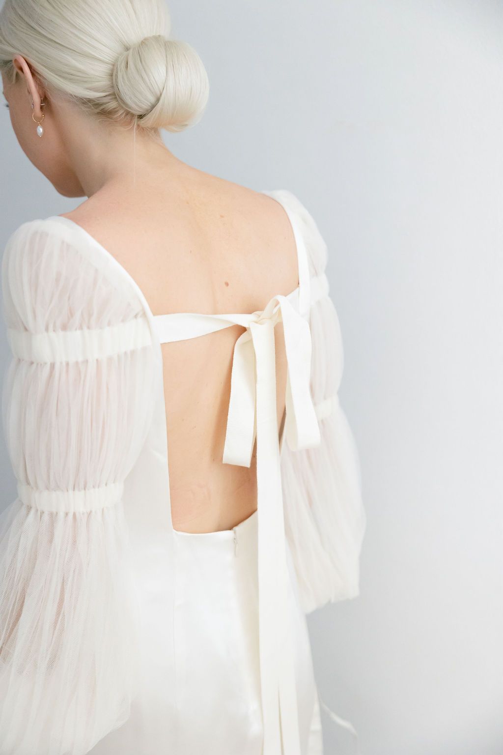 Detail shot of a sheer white wedding dress back with delicate tie closures and gathered fabric details.
