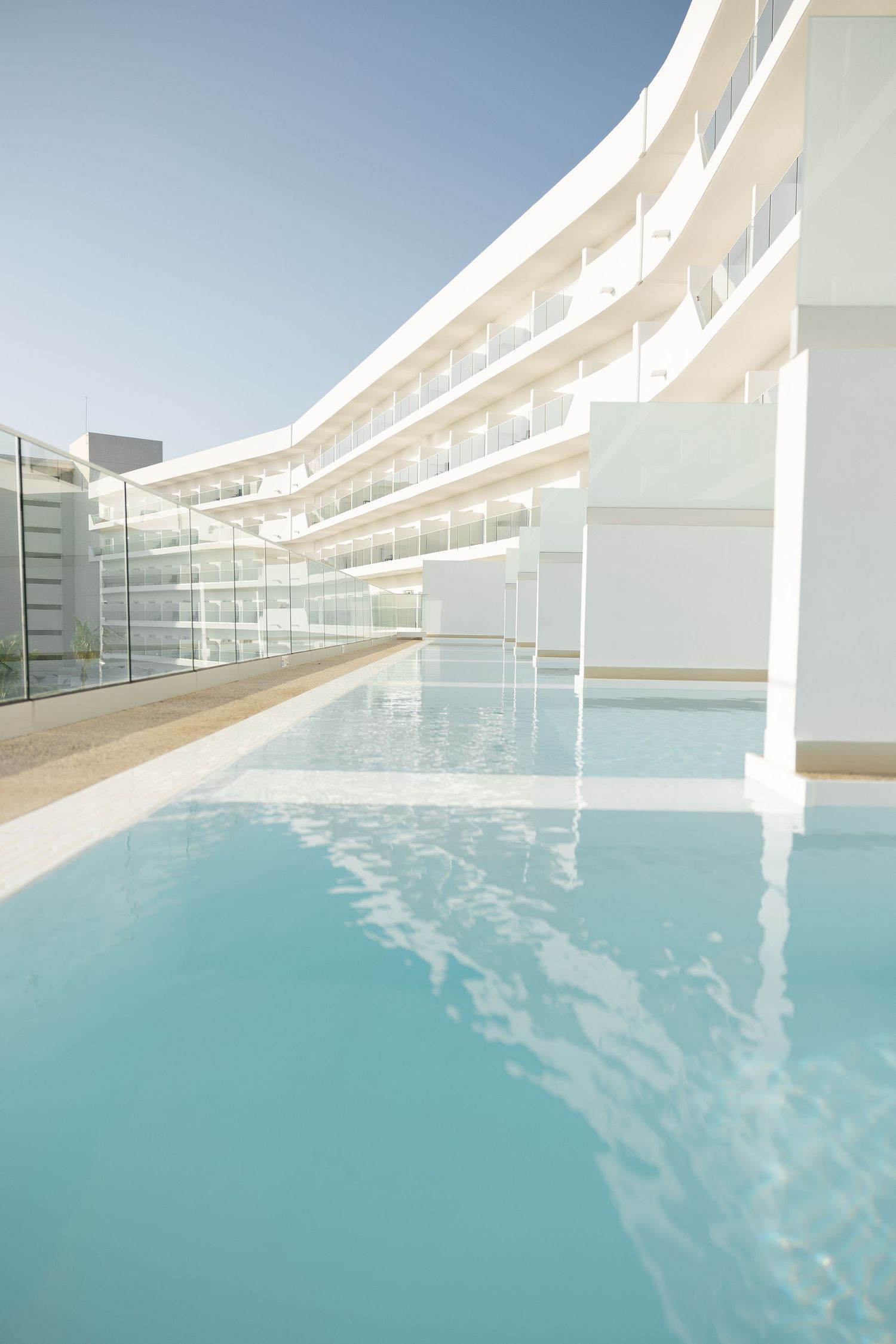Curved architectural balconies frame a luxurious rooftop swimming pool with azure waters.