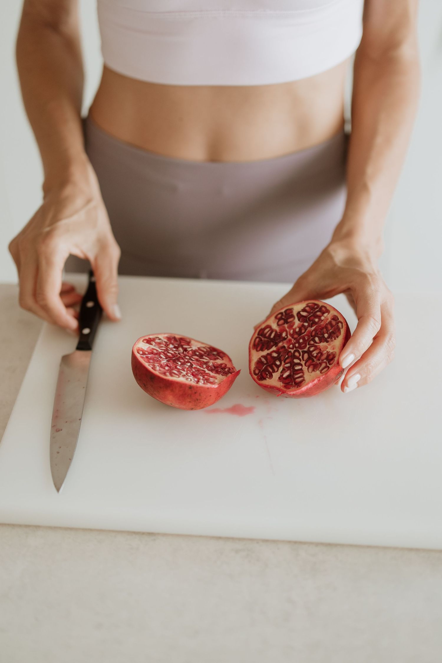 Hands cutting fresh pomegranate on white cutting board in bright kitchen.