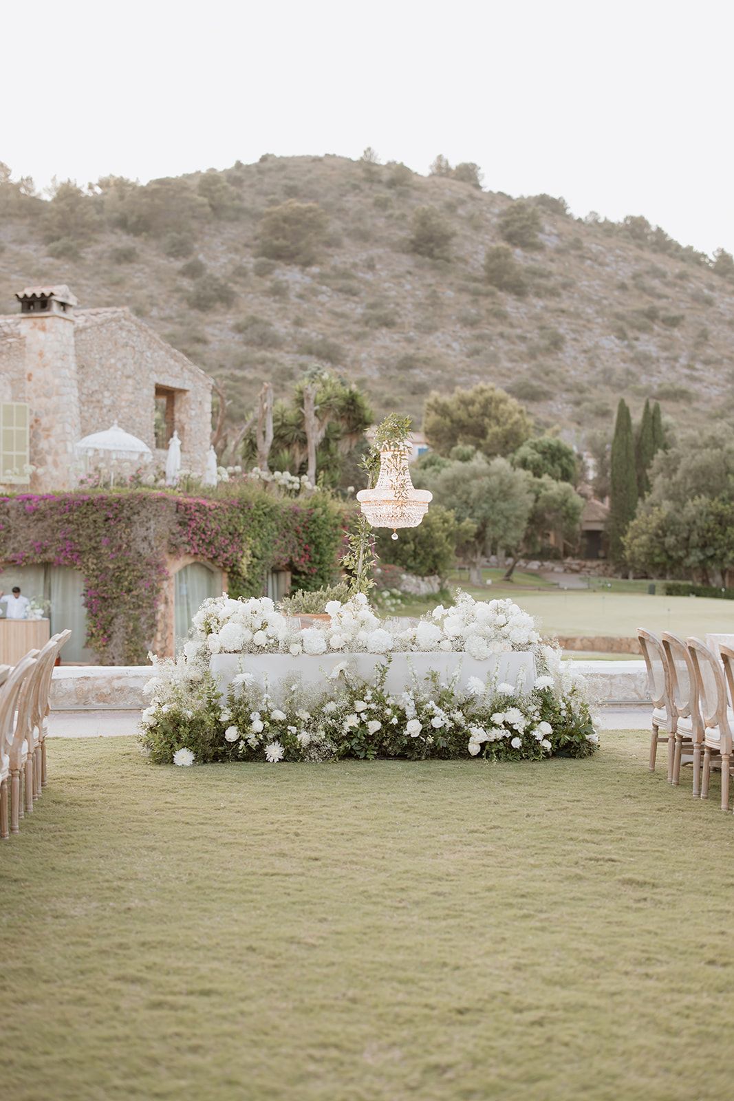 Outdoor wedding ceremony setup with white floral arrangements against a mountainous landscape.