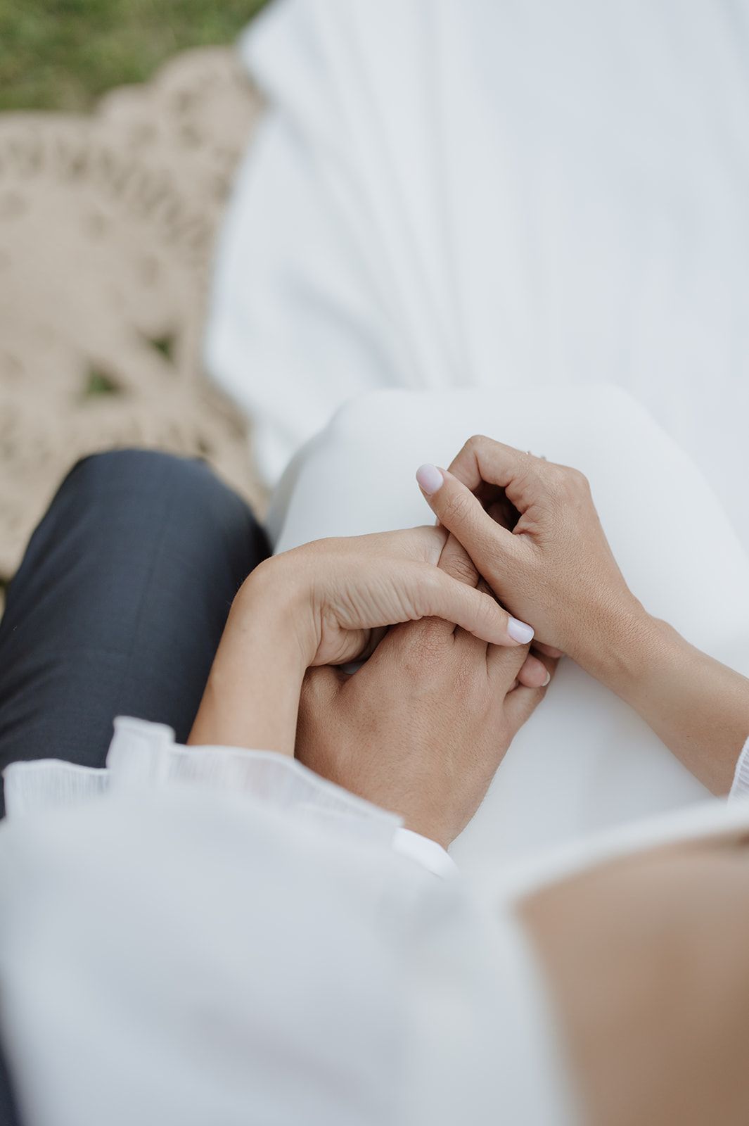 Close-up of hands gently clasped together against white fabric in an intimate wedding moment.