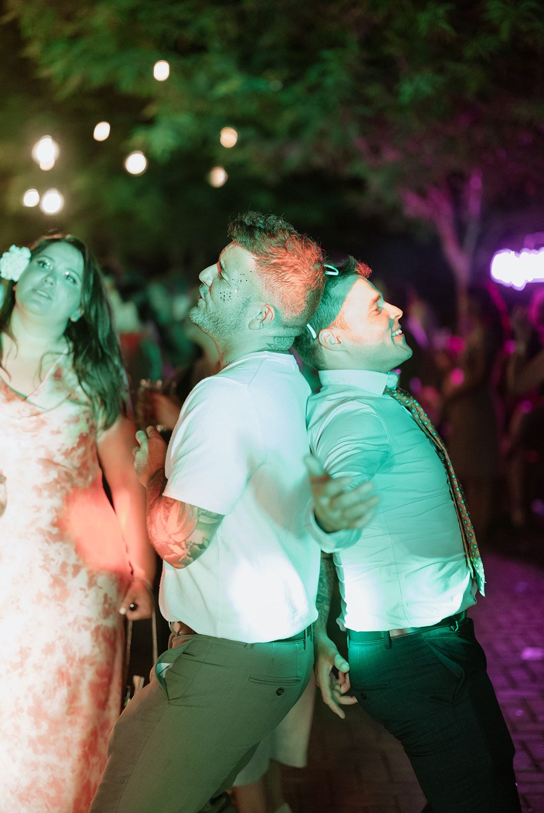 Party guests dancing in colorful lighting at an outdoor evening celebration.