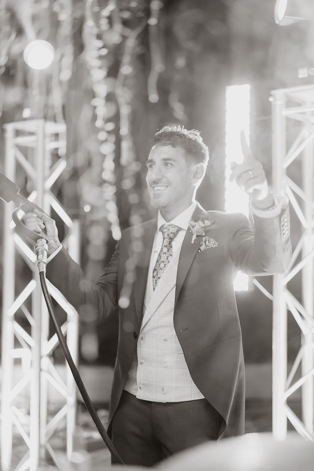 Well-dressed person celebrating with raised arms under decorative lighting.