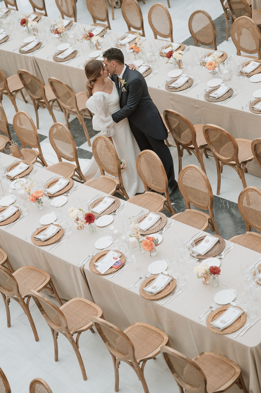 Wedding reception venue setup with elegant tan chairs and white tablecloths in a modern space.