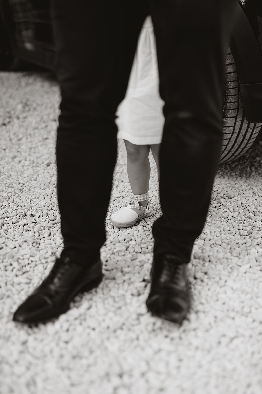 Black and white photo contrasting adult dress shoes with small white children's shoes.