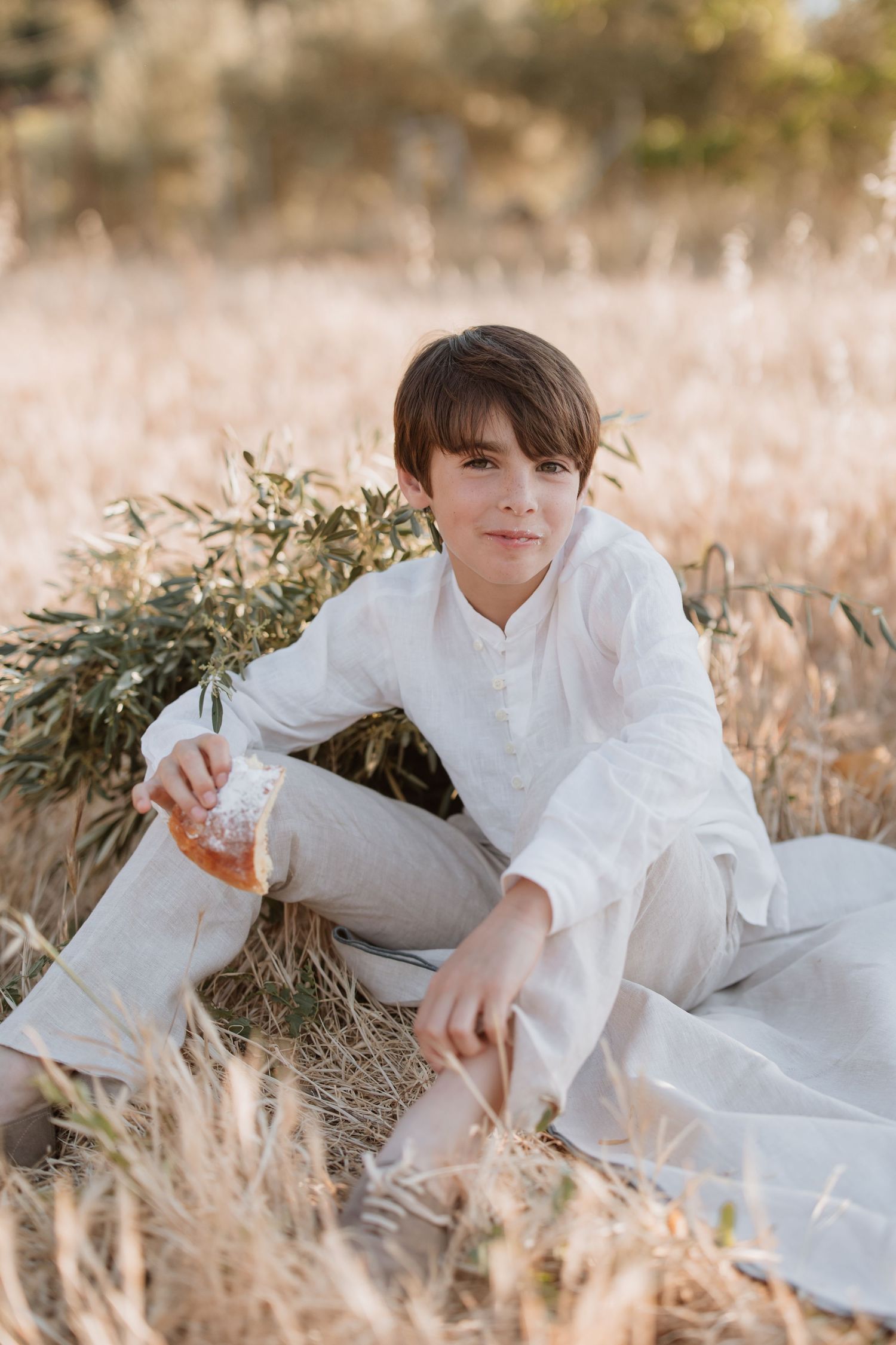 Person in white clothing sitting in a sun-lit field of tall golden grass during golden hour.