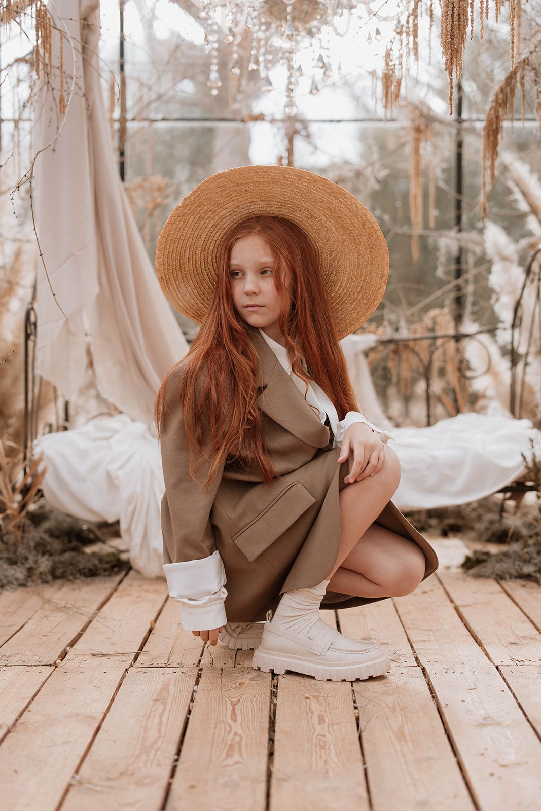 Natural light portrait with straw hat and oversized coat in greenhouse setting.