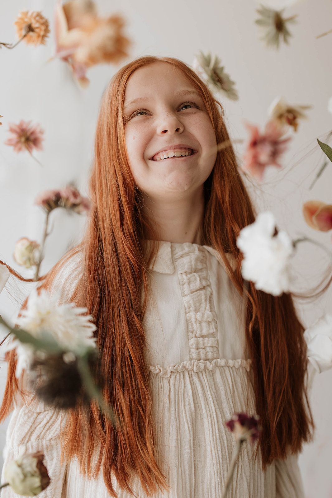 Gentle portrait with flowing copper hair and white dress against floral background.