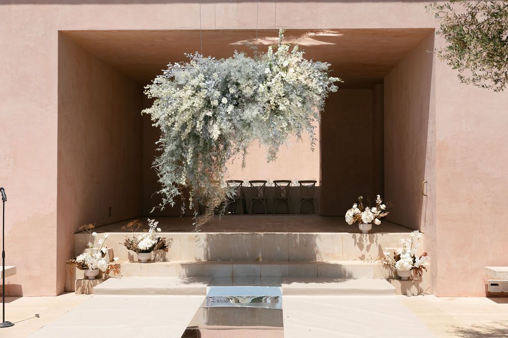 Wedding ceremony arch decorated with dusty blue florals against a pink stucco wall.