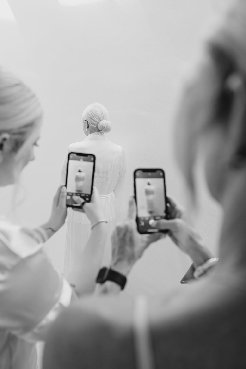 People taking photos with smartphones in a bright white setting.