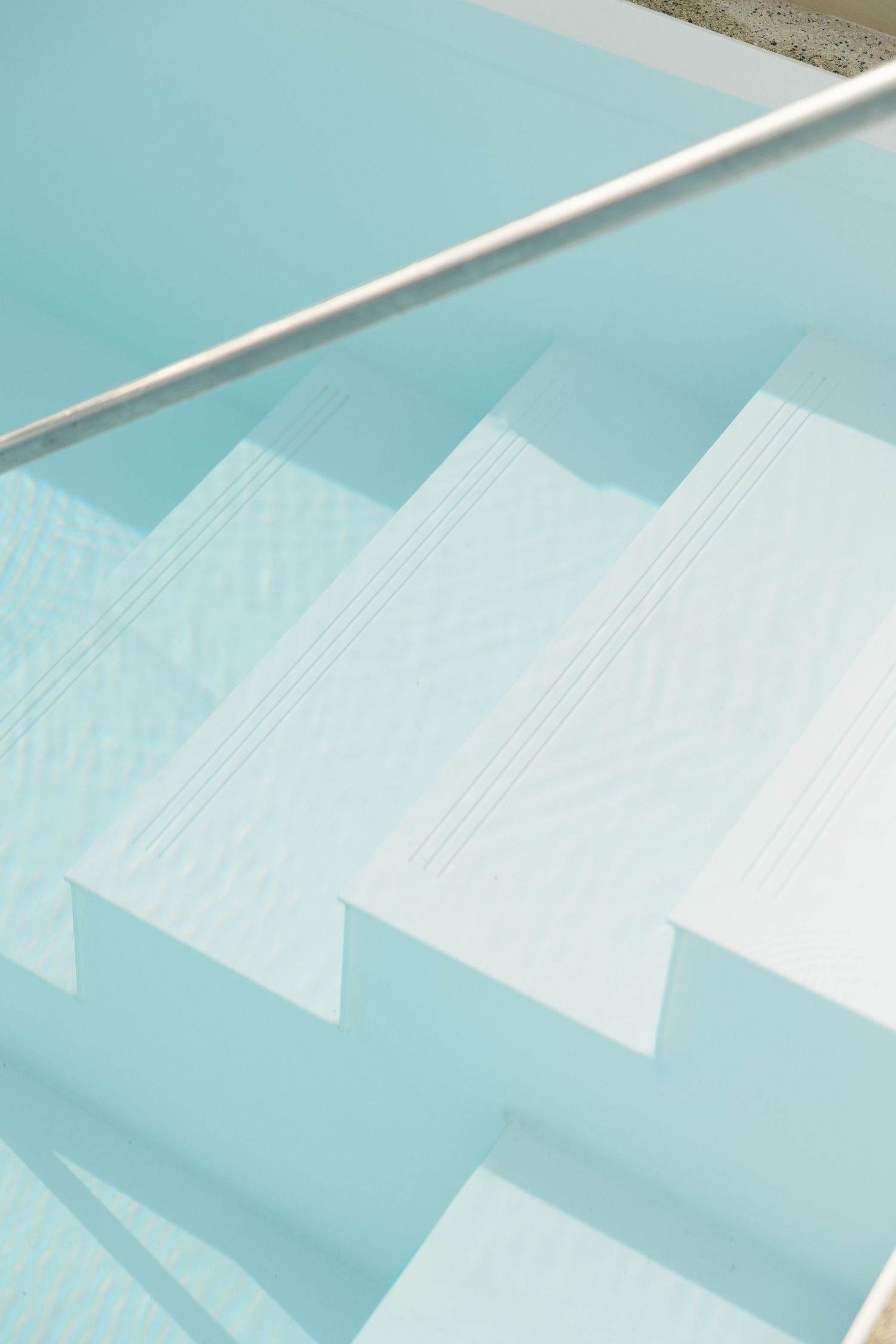 White pool steps descending into turquoise water with metallic handrail.