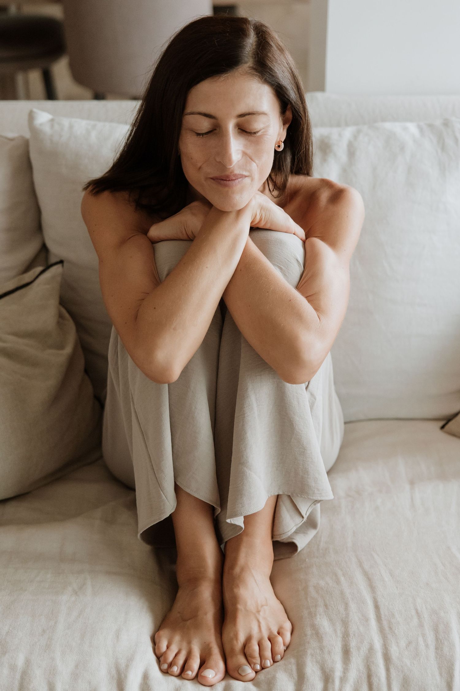 Natural light portrait of person in neutral tones sitting on white couch.